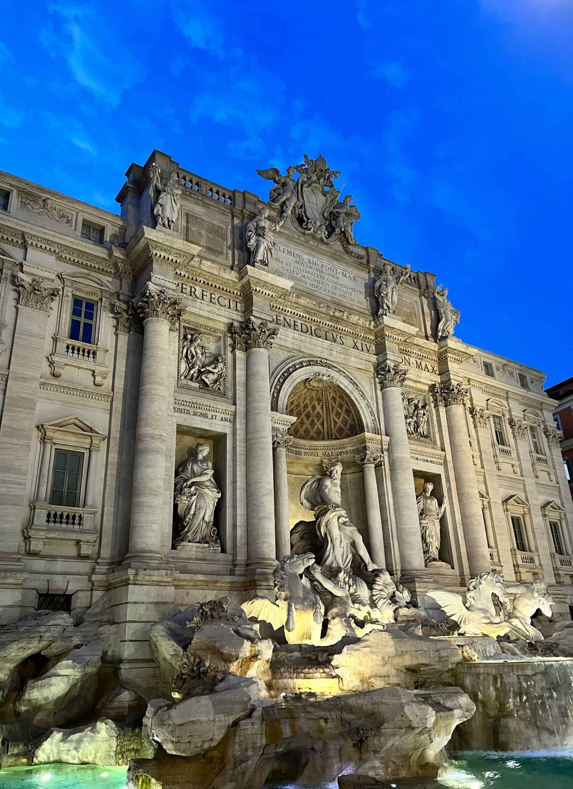 Trevi Fountain Rome at night with illuminated baroque sculptures and dramatic blue evening sky