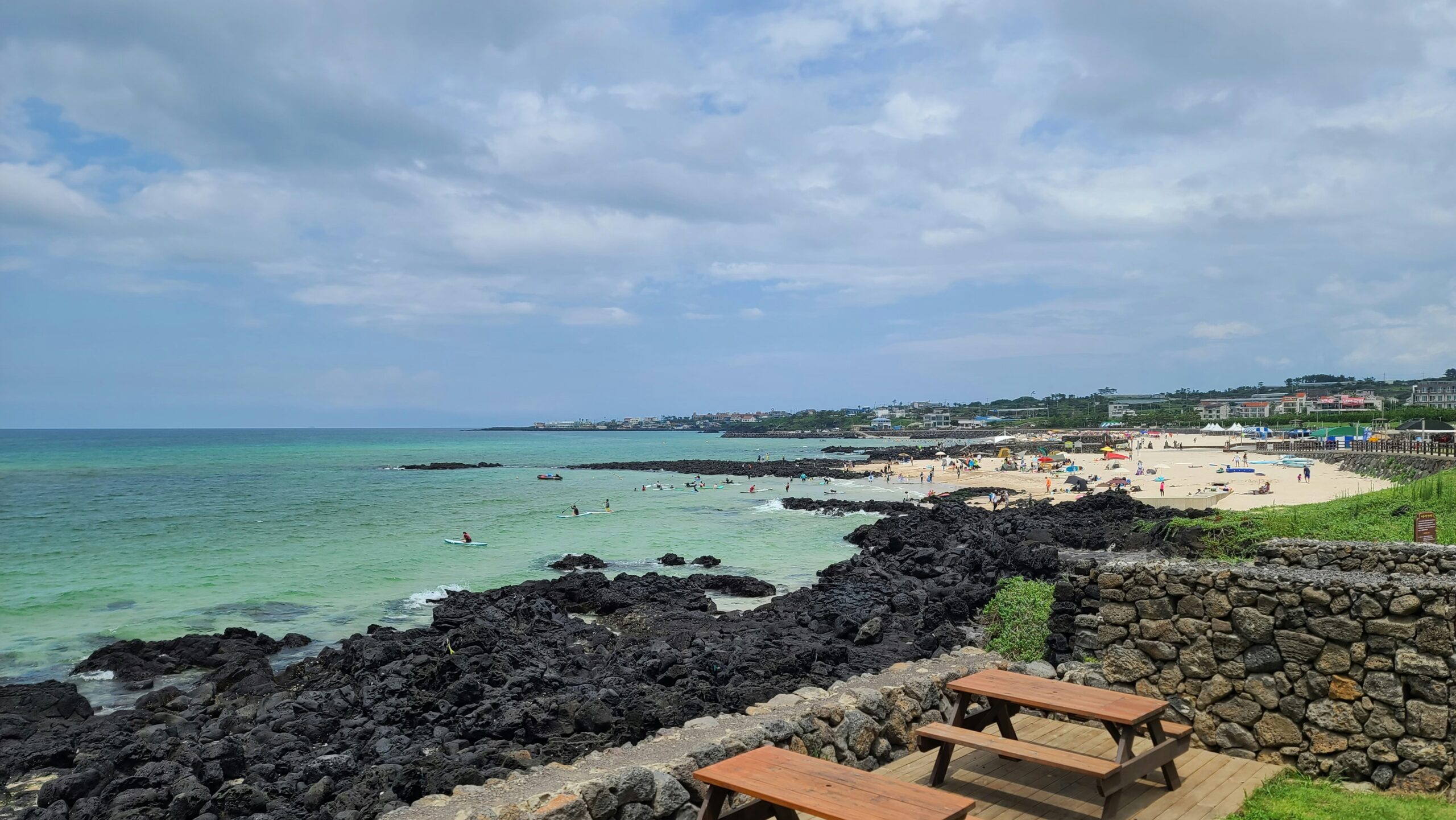 Coastal view in Jeju with emerald water, black volcanic rocks, and a seaside promenade