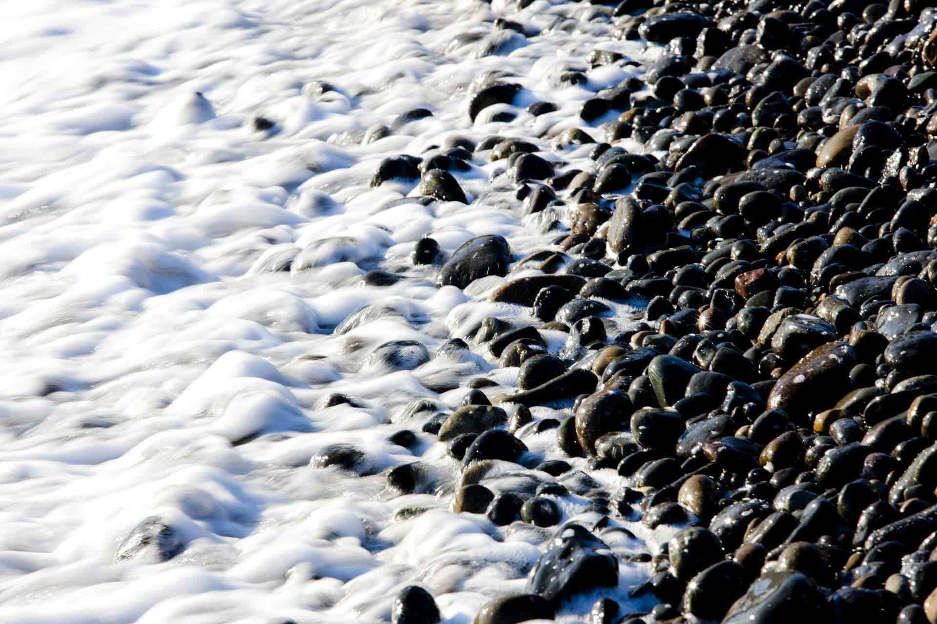 Hakdong Mongdol Beach black pebble stones with sea waves washing over them in Geoje South Korea