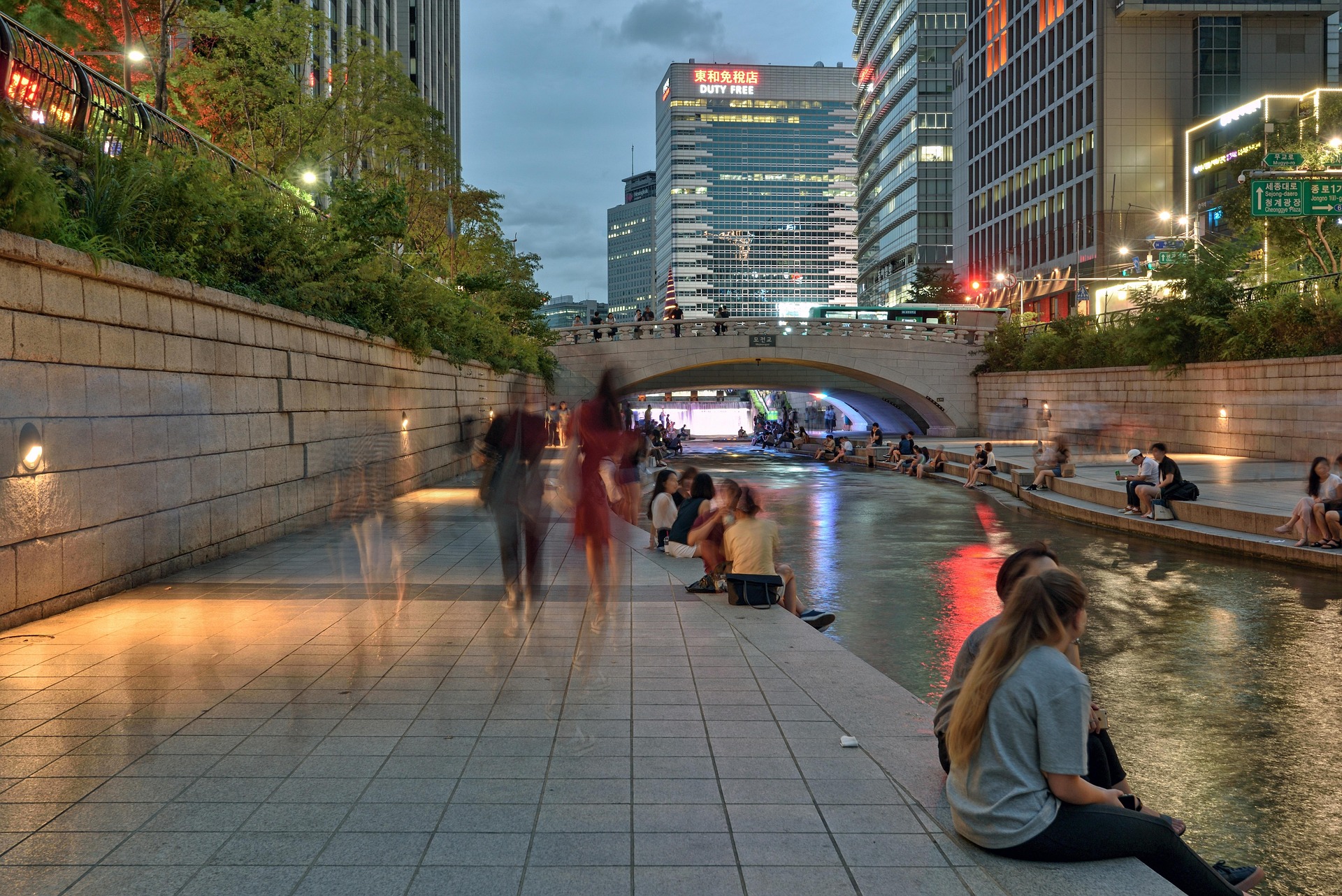 Cheonggyecheon Stream walkway in Seoul at dusk with city lights and people relaxing by the water