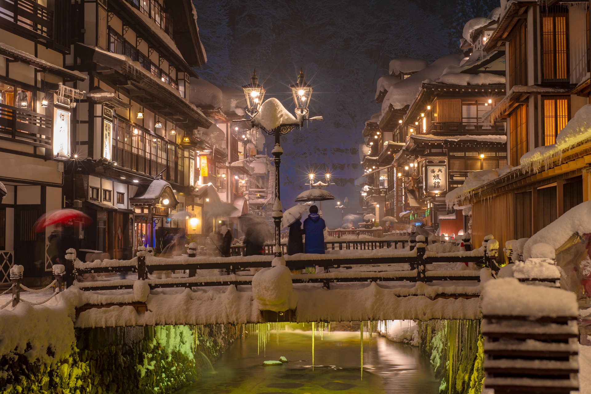 Ginzan Onsen snowy night street with traditional ryokan and illuminated bridge in Yamagata Japan