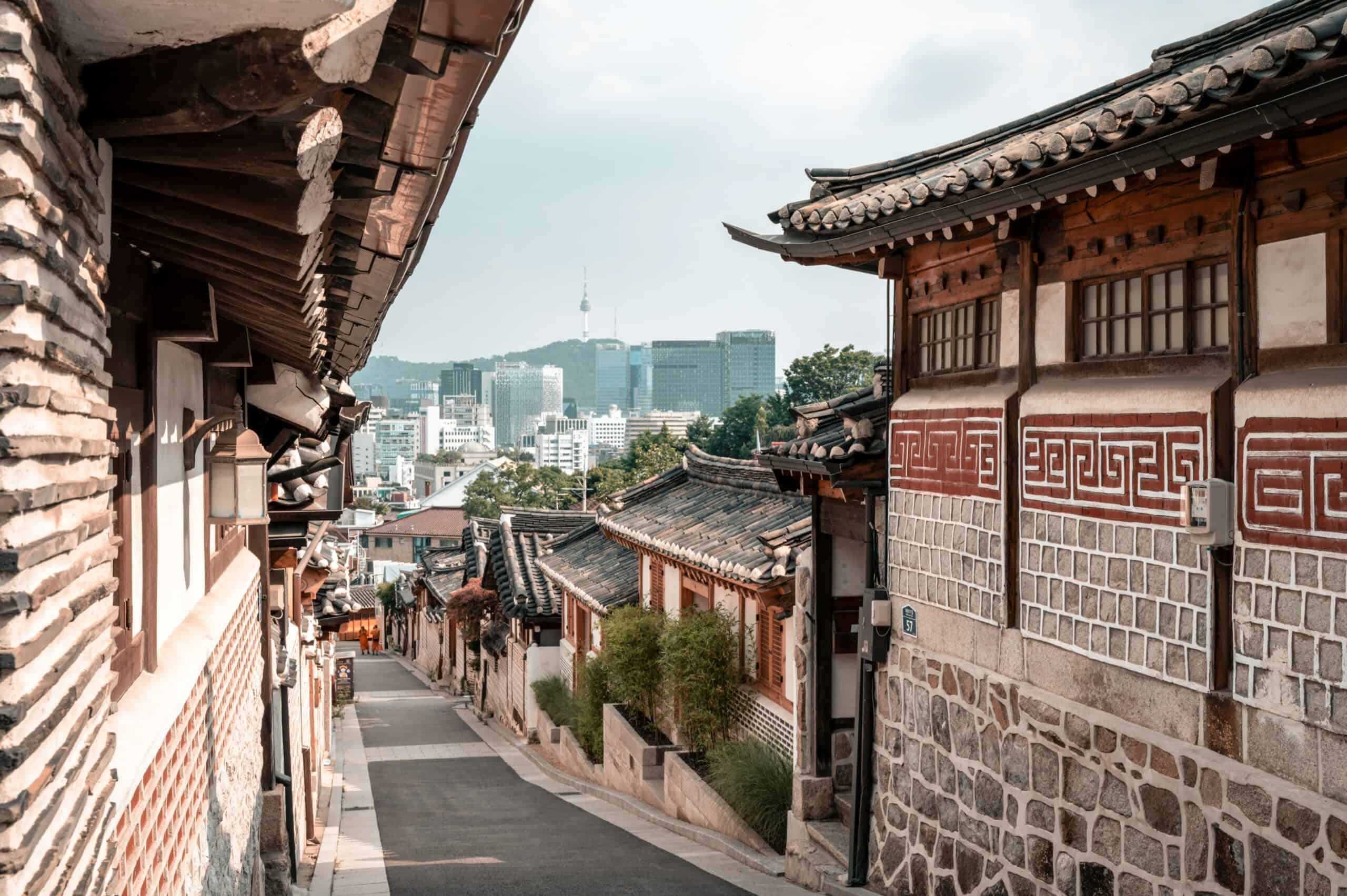 Bukchon Hanok Village traditional alley with hanok rooftops and Seoul skyline in the background